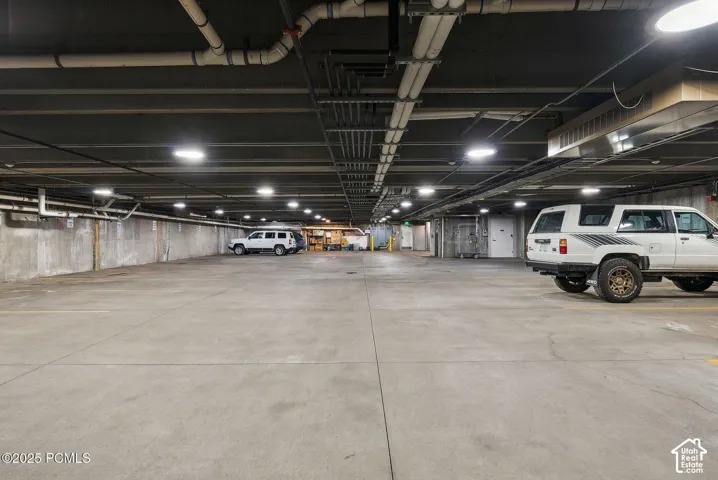 Spacious underground parking area with concrete flooring, exposed ceiling utilities, and ample overhead lighting