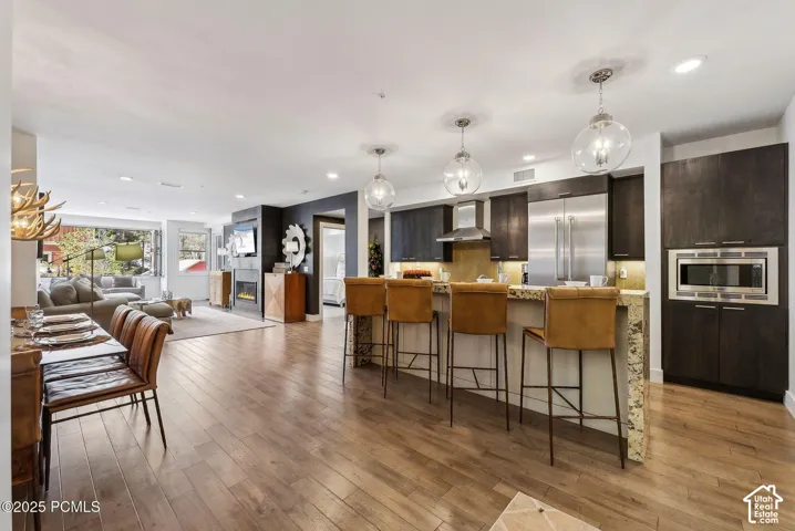 Wood-finish flooring throughout, kitchen with stone countertops and stainless steel appliances, built-in microwave, dark wood cabinetry, and recessed lighting