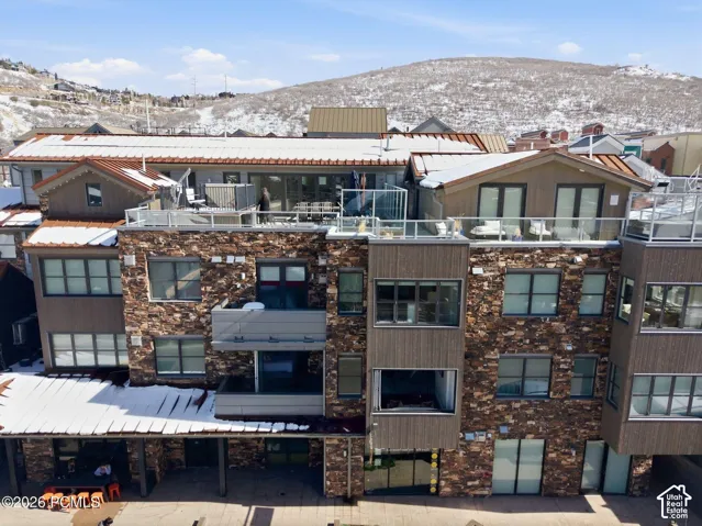 Multi-level building exterior featuring stone and wood-panel accents, multiple private balconies, and a rooftop terrace with glass railings