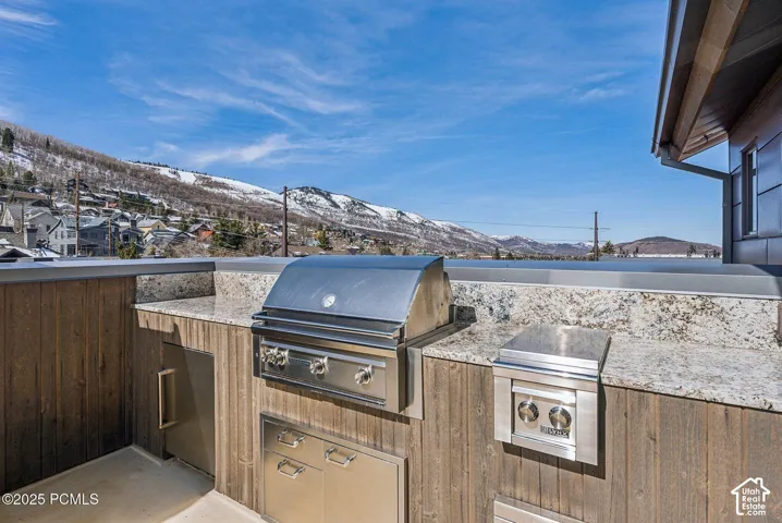 Outdoor kitchen with stainless steel grill, side burner, and cabinetry, set against a snow-dusted mountain backdrop