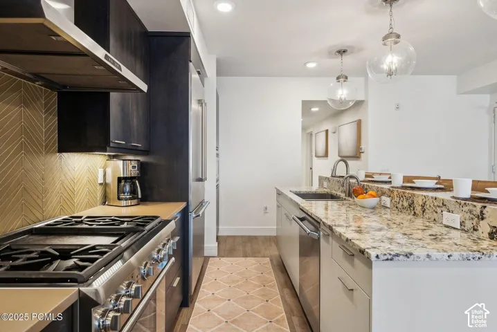 Chef's kitchen featuring a six-burner gas range with stainless steel hood, granite countertops with waterfall island edge, white cabinetry with soft-close drawers, herringbone tile backsplash, and pendant lighting