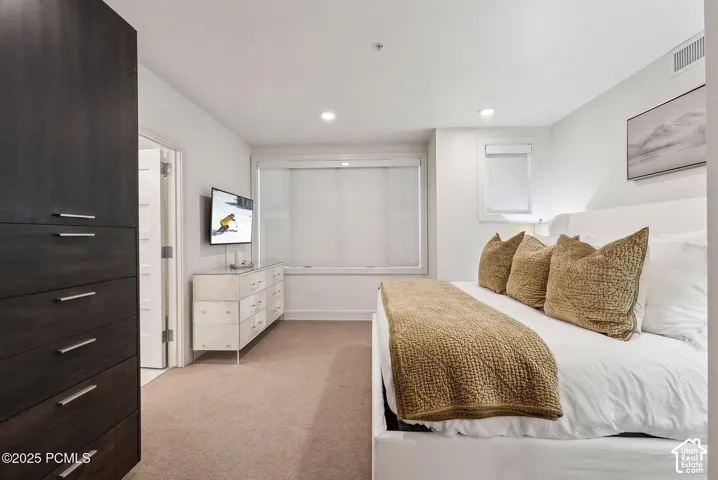 Integrated dark wood-finish cabinetry, recessed ceiling lighting, a broad window with roller shades, and plush carpeting
