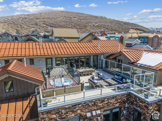Expansive rooftop deck featuring a hot tub, glass panel railings, a built-in fire pit, and a stone facade