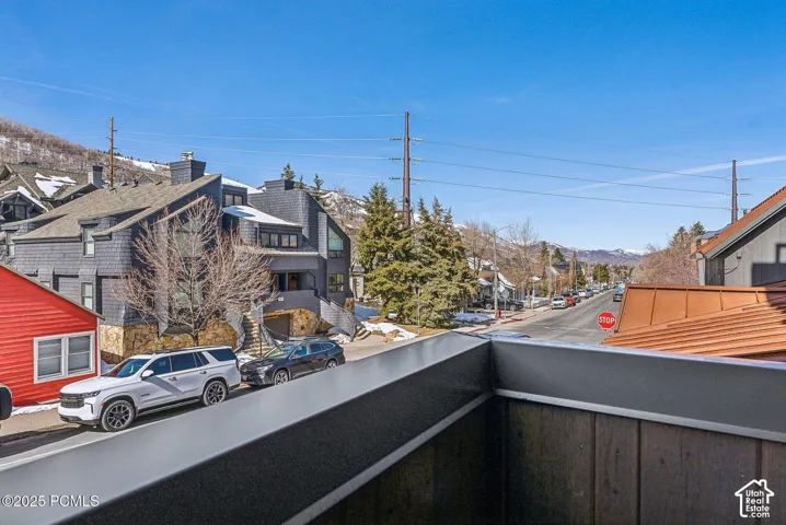 Balcony with wood-finish siding and metal railing overlooking a street with mountain backdrops