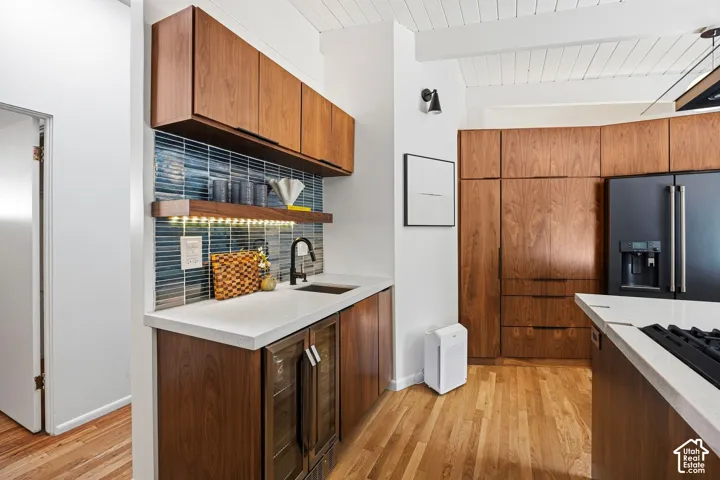 Wood-finish cabinetry, white countertops, blue tile backsplash, black faucet, and wood-finish flooring