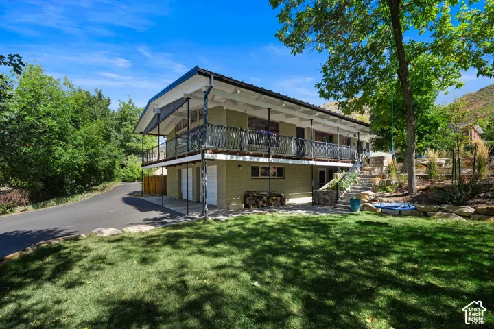 Two-story residence featuring a ground-level garage, upper-level balcony with a black metal railing, and a multi-tiered stone landscaping
