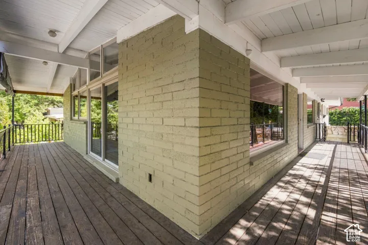 Expansive outdoor deck with wood flooring, painted brick exterior, white exposed beam ceiling, and a black metal railing