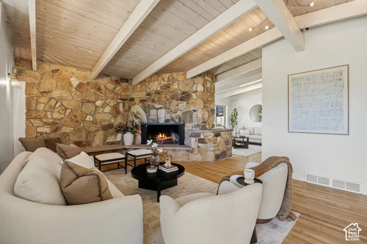 Exposed wood beam ceiling, stone-clad fireplace with hearth, hardwood flooring, and recessed lighting