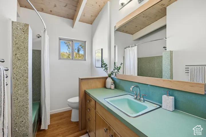 Vaulted wood-plank ceiling, wood-finish flooring, built-in wood cabinetry, integrated basin sink, and a tiled shower-bath combination