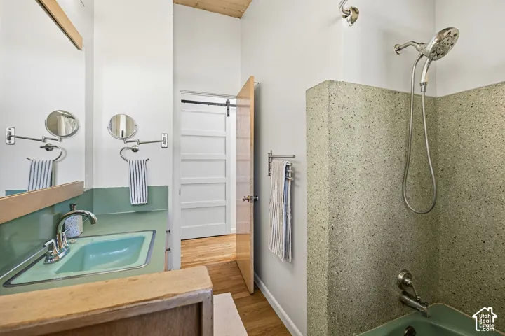Terrazzo-style shower surround, chrome shower fixtures, wood-finish flooring, accent wall with integrated basin, paneled sliding barn door