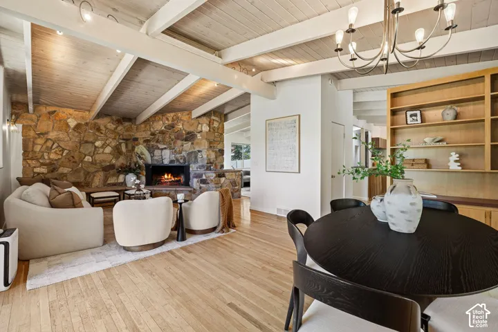 Exposed beam ceiling with wood paneling, natural stone fireplace, wide plank wood flooring, built-in shelving, and a modern chandelier