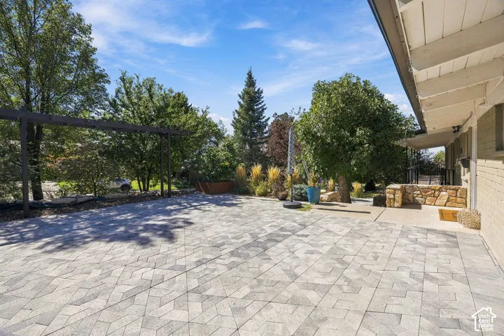 Expansive paver patio with a geometric pattern, surrounded by mature trees and a wood pergola