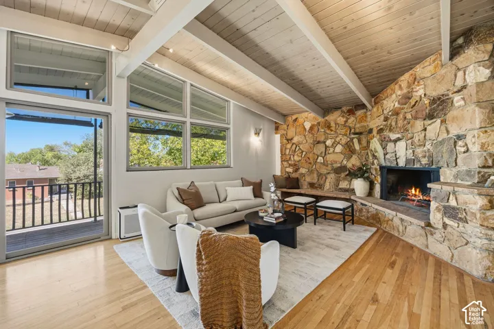 Vaulted wood-paneled ceiling with exposed beams, natural stone fireplace, large sliding glass door, and multiple upper windows