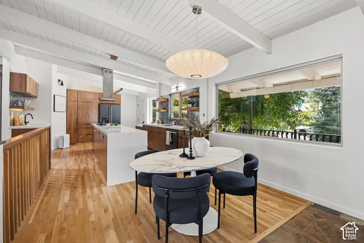 Exposed beam ceiling, wood-finish flooring, built-in wooden cabinetry, white quartz kitchen island, and a wide horizontal window