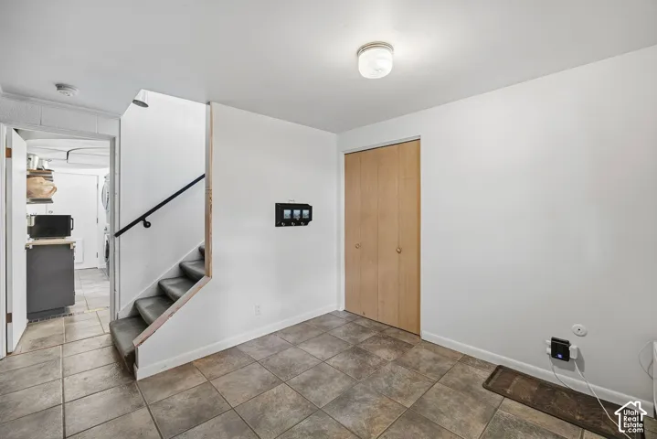 Tile flooring, light wood-finish bi-fold closet doors, white walls, and a staircase with a black handrail