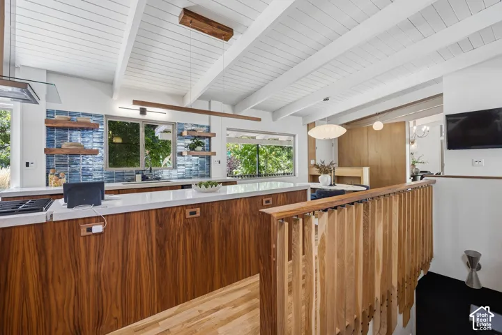 Vaulted white plank ceiling, wood-finish cabinetry, white countertops, blue subway tile backsplash, and wood-finish open shelving
