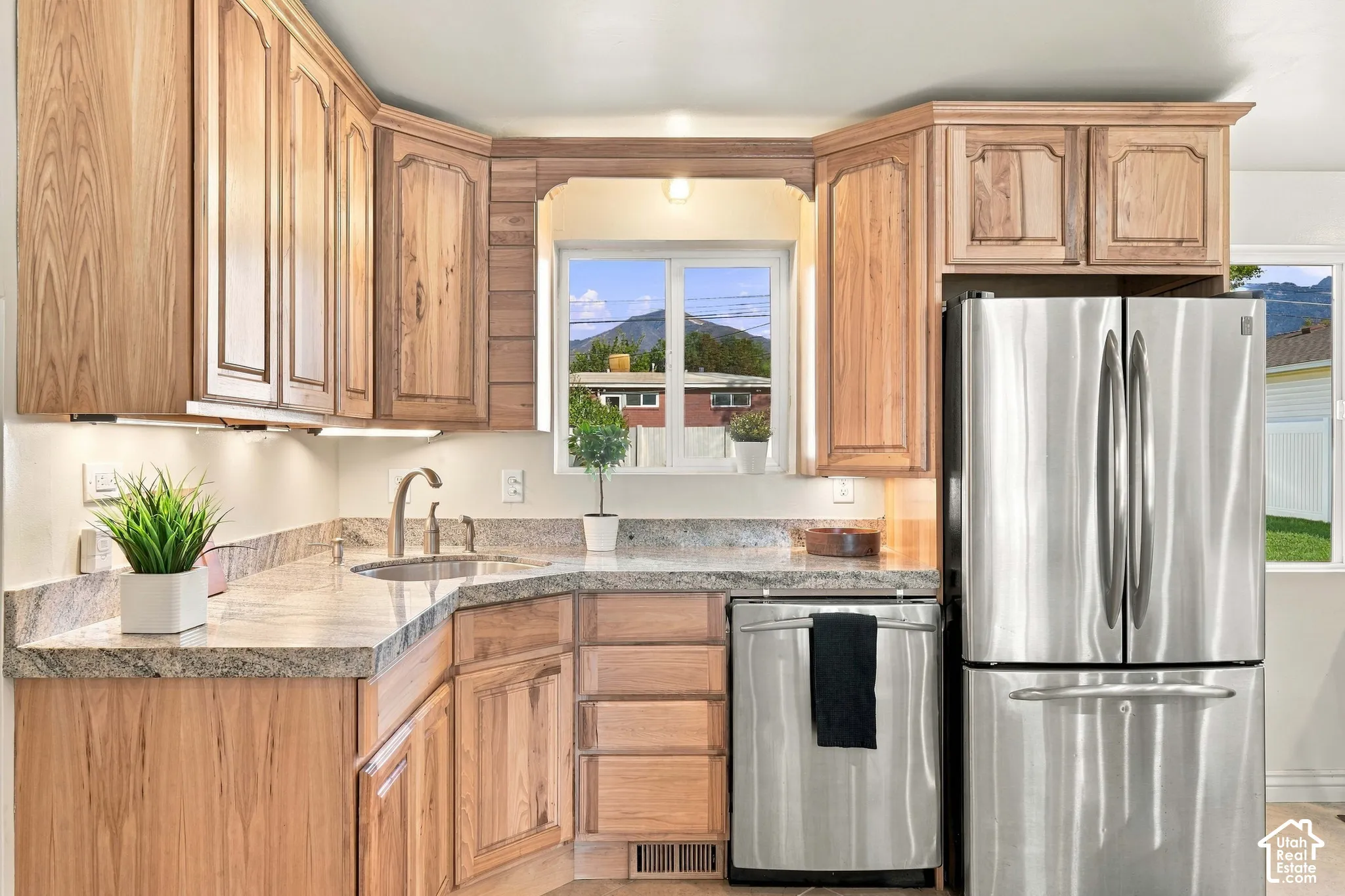L-shaped kitchen with natural wood cabinetry, light-toned countertops, under-cabinet lighting, and stainless steel appliances