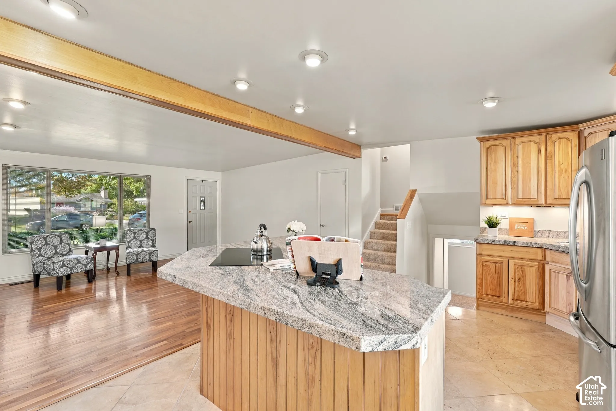 Kitchen island with granite countertop, wood-finish cabinetry, stainless steel refrigerator, and recessed lighting