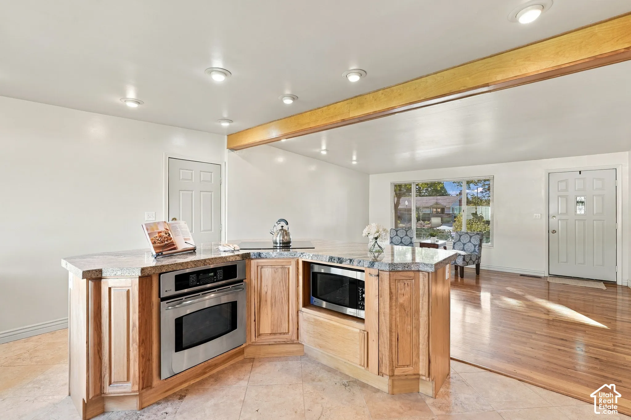 Kitchen island with light wood-finish cabinetry, integrated stainless steel appliances, and a granite countertop