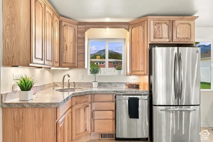 L-shaped kitchen with natural wood cabinetry, light-toned countertops, under-cabinet lighting, and stainless steel appliances