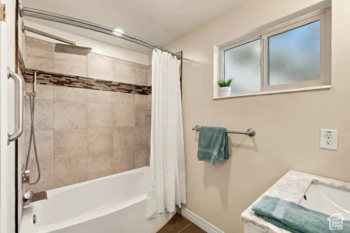 Bathtub with a tiled surround featuring a decorative mosaic accent, rainfall showerhead, and grab bar