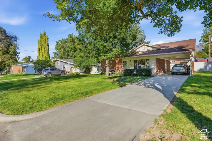 Brick and siding exterior with a covered carport, mature trees, and a concrete driveway