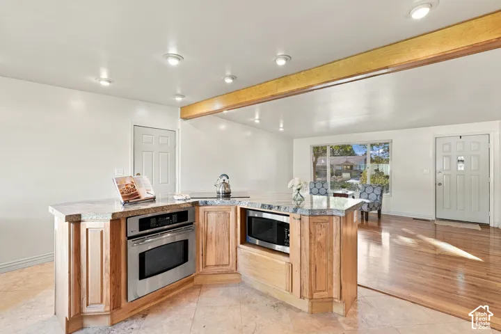 Kitchen island with light wood-finish cabinetry, integrated stainless steel appliances, and a granite countertop