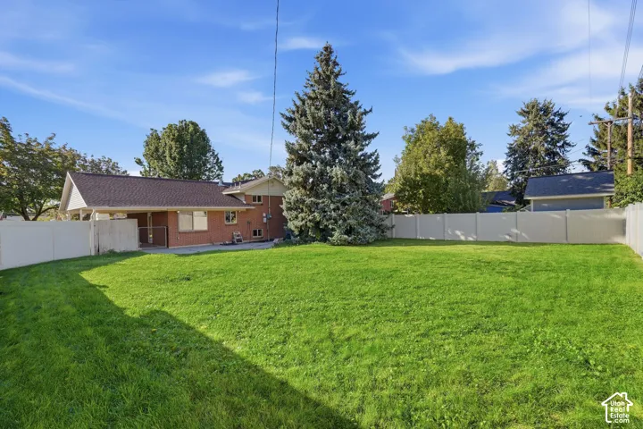 Expansive grassy yard with a privacy fence, mature trees, and a brick exterior dwelling with a covered patio area