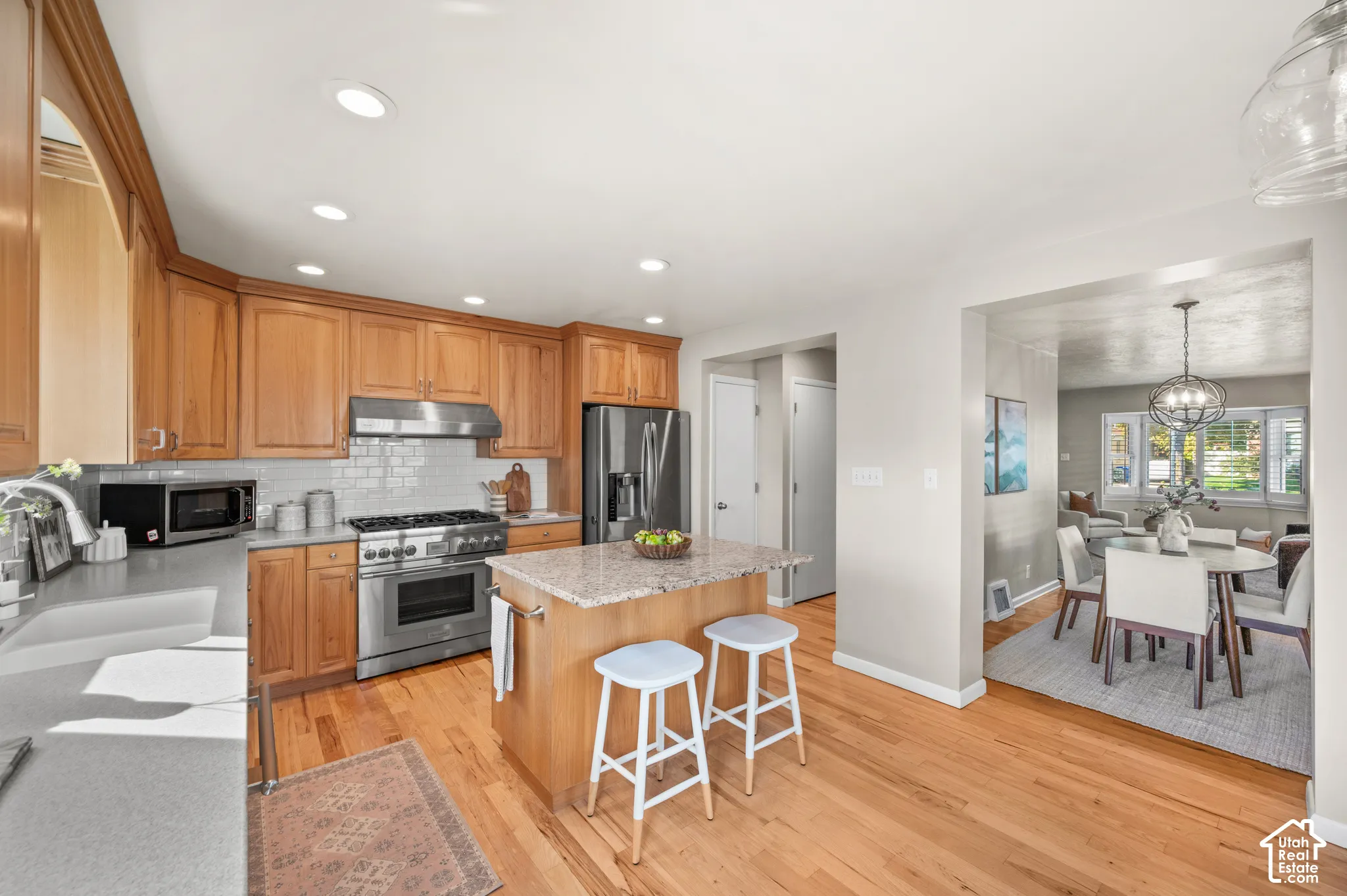 Kitchen featuring wood cabinetry, stone-surface island, stainless steel range with a mounted vent hood, subway tile backsplash, and wood-finish flooring