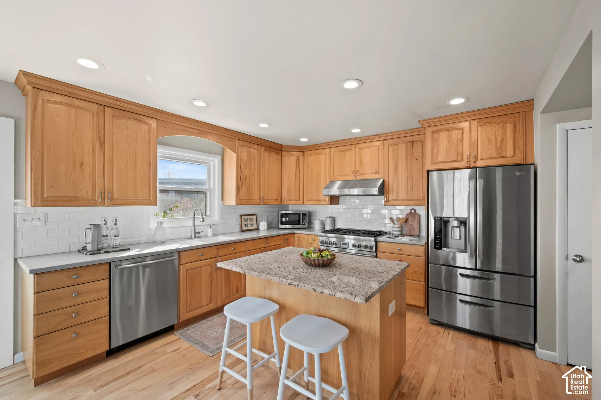 Kitchen featuring wood cabinetry, natural stone countertops, stainless steel appliances, recessed lighting, and wood-finish flooring