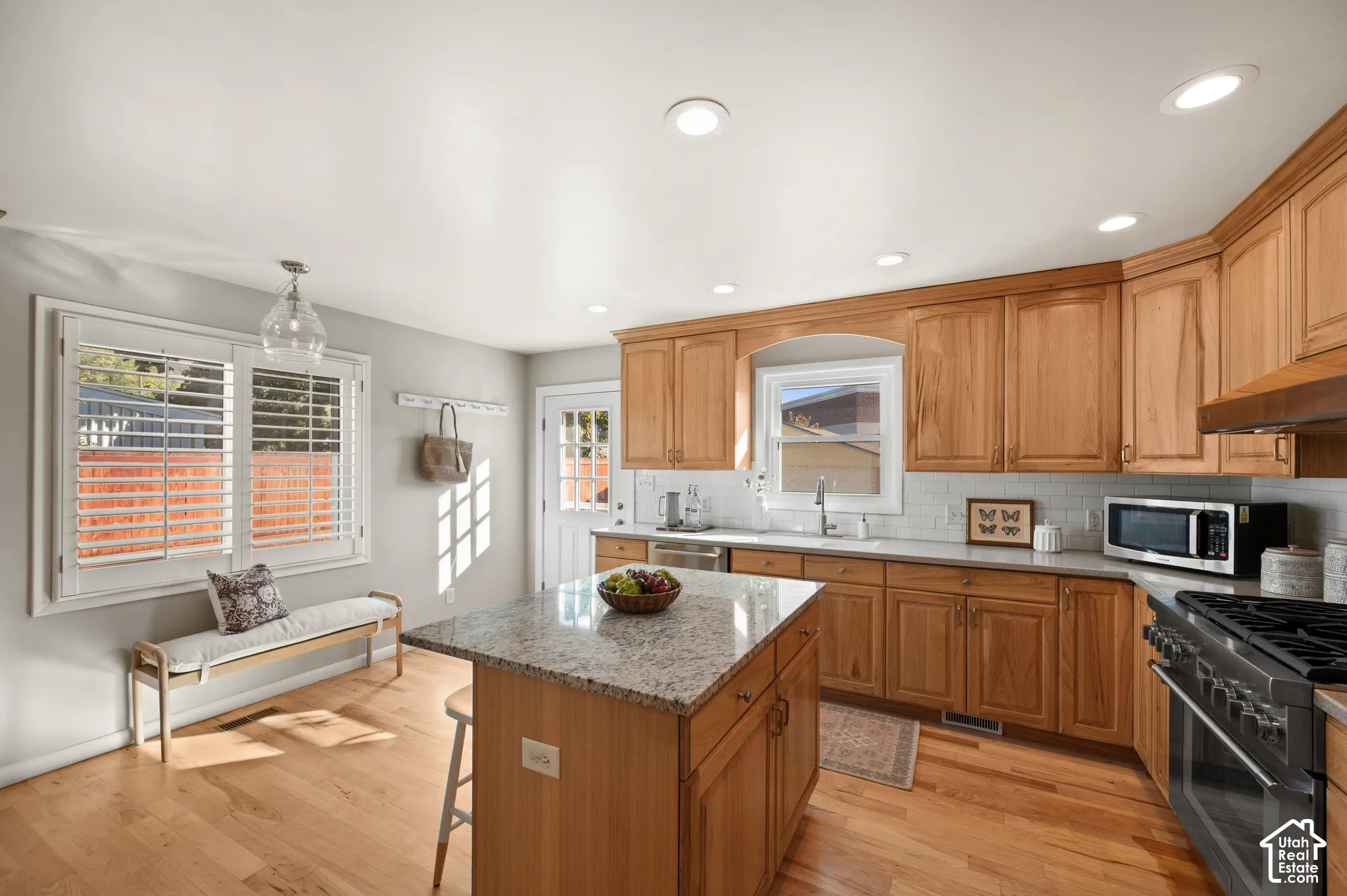 Kitchen featuring natural wood cabinetry, stone-surface kitchen island, subway tile backsplash, wood-finish flooring, and recessed ceiling lighting