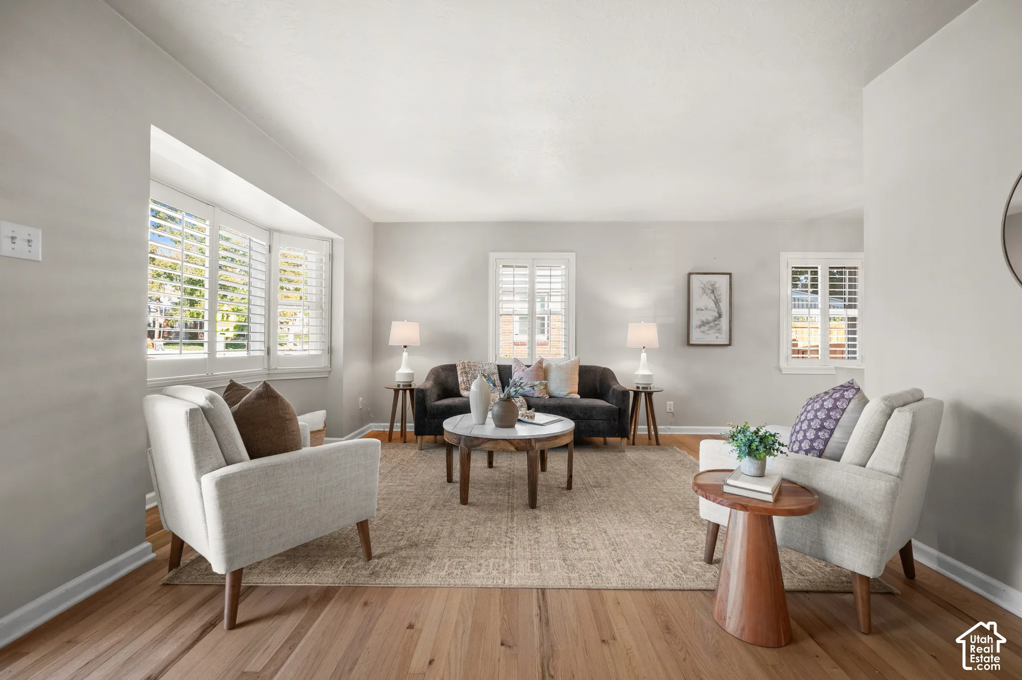 Living space featuring wood-finish flooring, a prominent bay window, and white plantation-style shutters