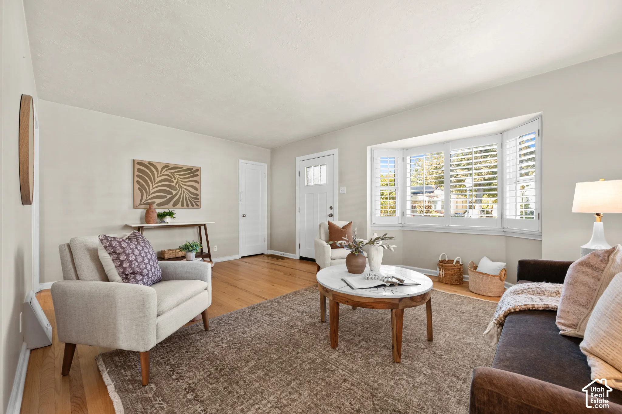 Living area featuring wood-finish flooring, a prominent bay window, and white plantation shutters