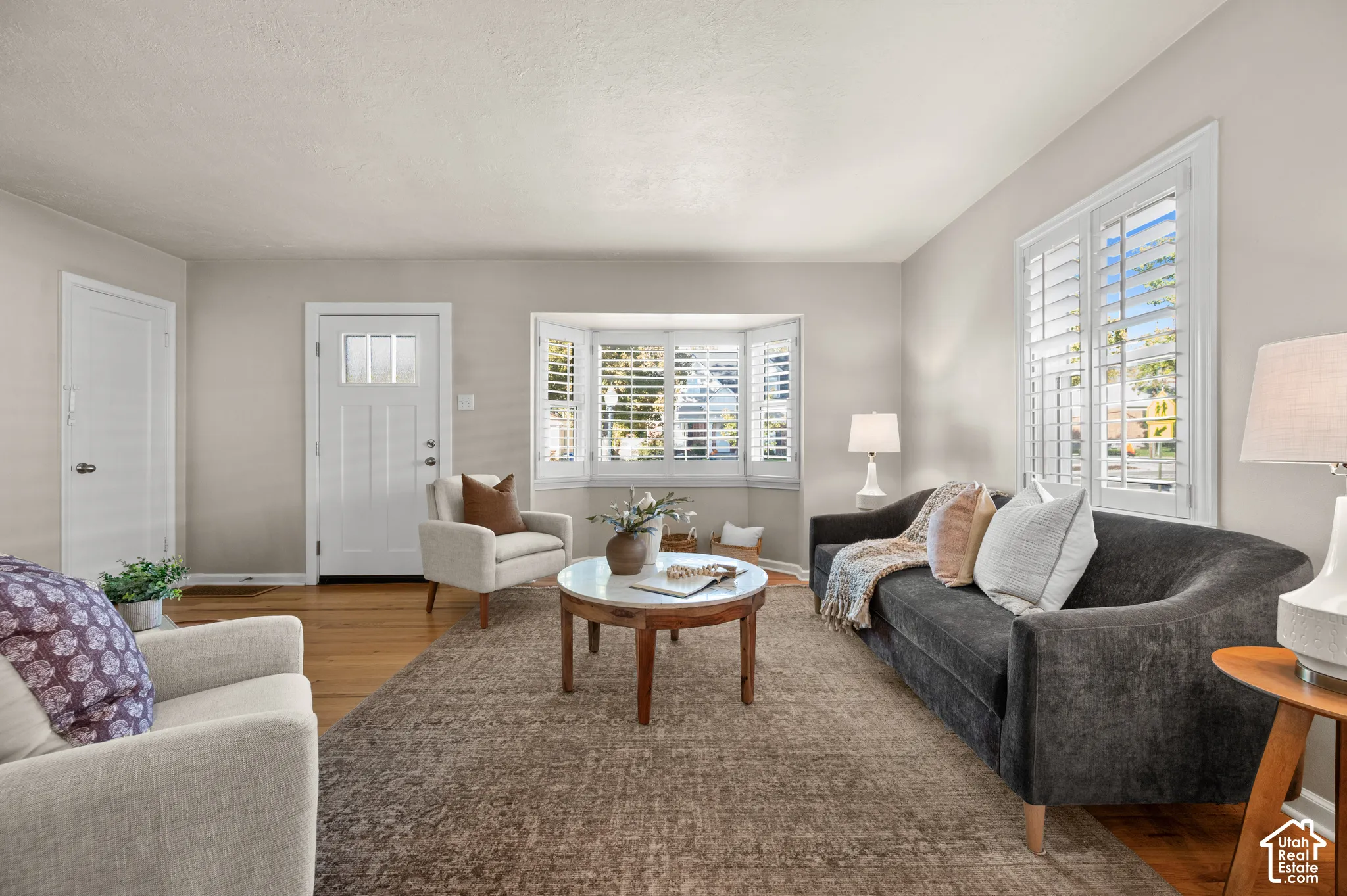 Living area featuring wood-finish flooring, a bay window with plantation shutters, and a multi-panel exterior door with glass insert