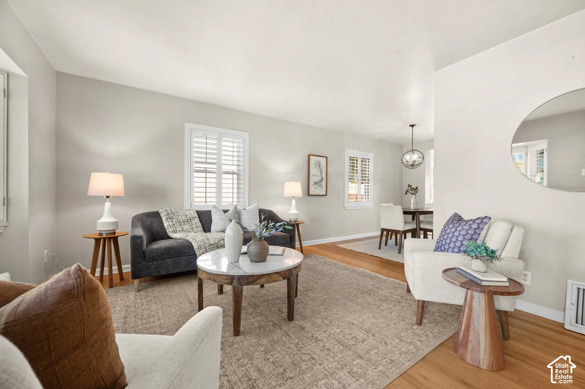 Living area featuring wood-finish flooring, white plantation shutters, and a circular wall mirror