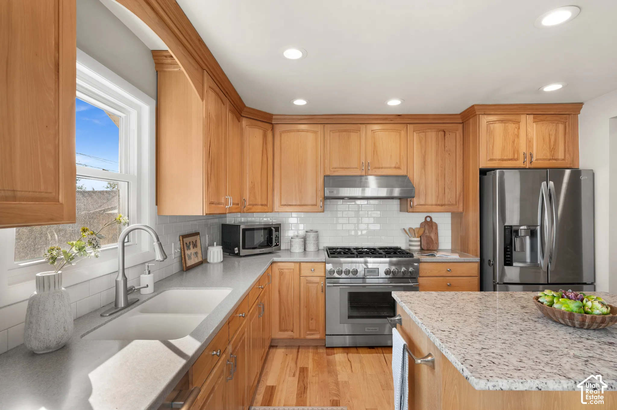 Kitchen featuring natural wood cabinetry, stone countertops, stainless steel gas range with a matching vent hood, and wood-finish flooring