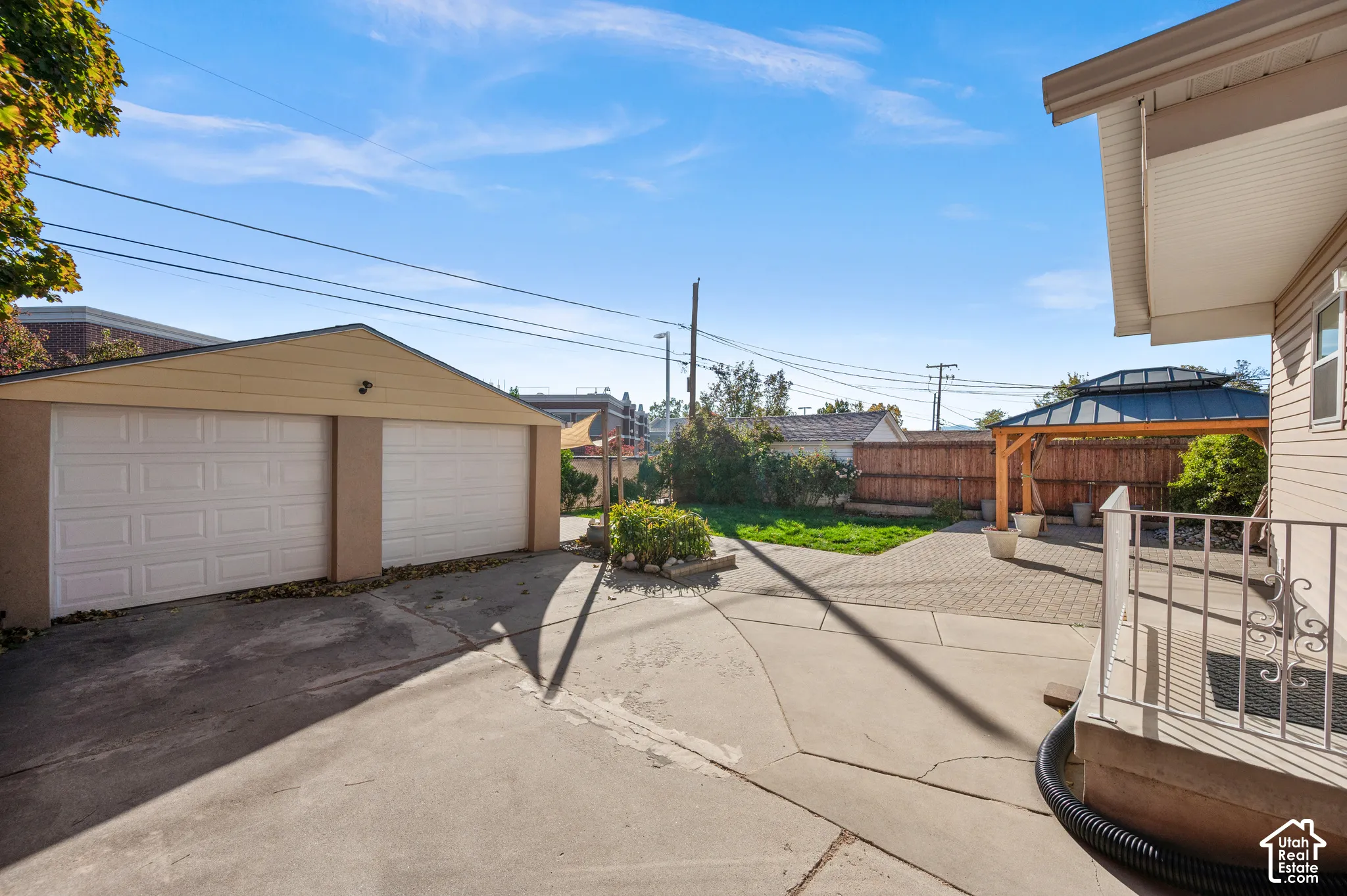 Backyard featuring a detached two-car garage, paved concrete driveway, stone paver patio, wooden gazebo, and perimeter privacy fencing