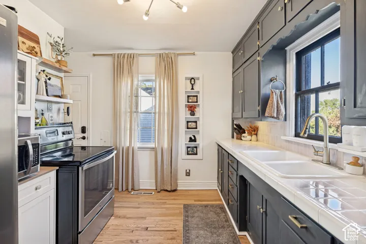 Kitchen featuring dark cabinetry with gold-finish hardware, a double basin sink, and a tiled countertop