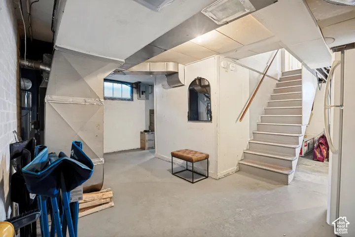 Concrete flooring with white painted walls, exposed ductwork, a multi-pane window, and a painted staircase featuring a wood handrail