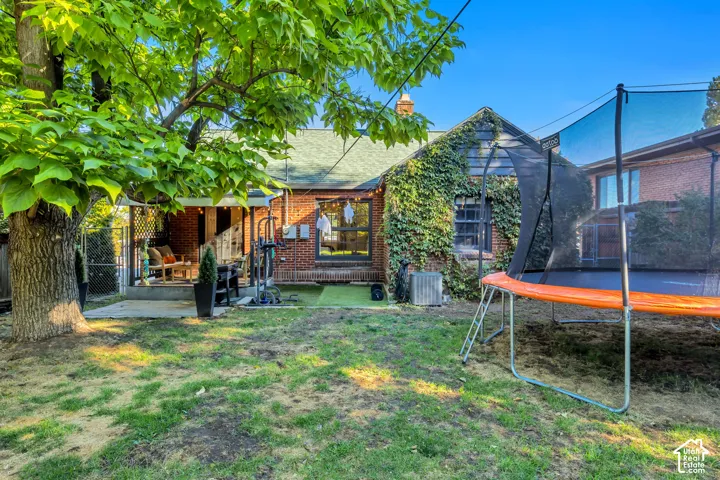 Expansive backyard featuring a mature tree, brick exterior, and covered patio