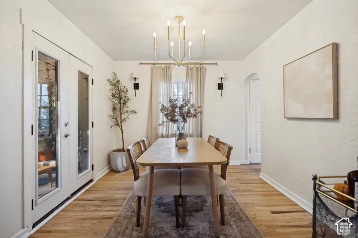 Light wood-finish flooring, white double French doors with glass panels, arched entryway, and a gold-finish chandelier