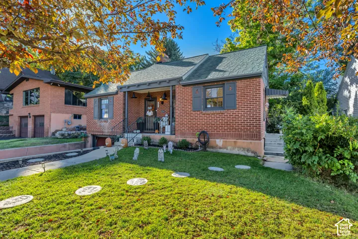 Brick exterior featuring a covered front porch, dark green roof shingles, and contrasting dark shutters