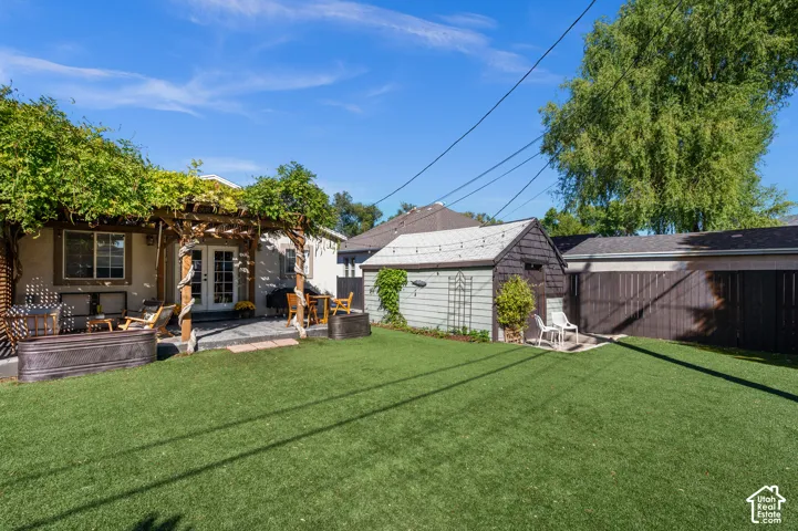 Expansive artificial turf backyard featuring a covered patio with a wood pergola, French doors, and a detached structure