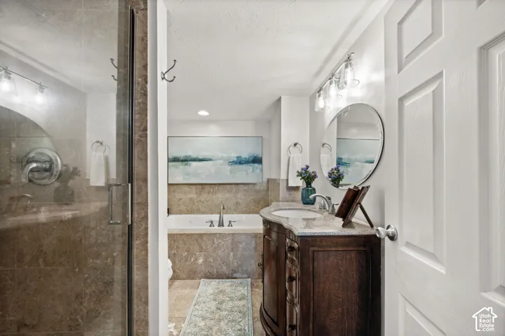Glass-enclosed shower with tile surround, freestanding bathtub, wood-finish vanity with countertop, and a circular wall mirror