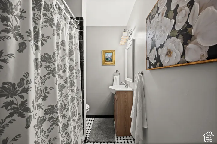 Pedestal sink with wood-finish vanity, wall-mounted light fixture, and black and white checkerboard flooring
