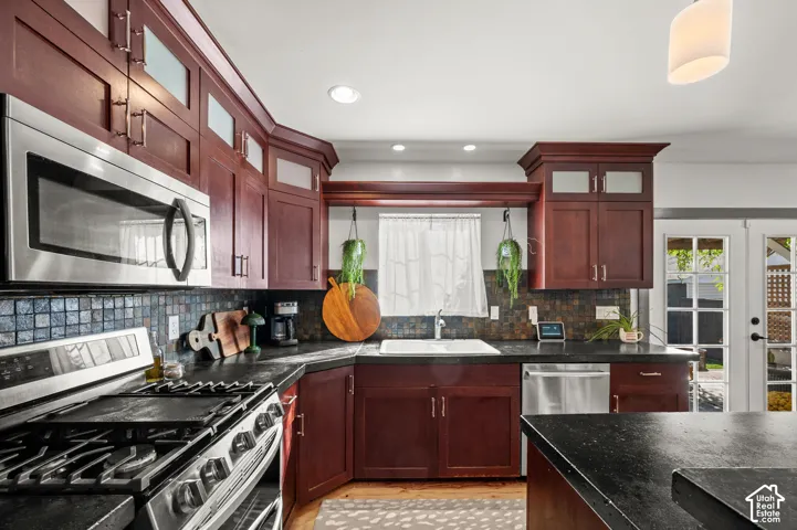 Kitchen featuring cherry wood cabinetry, stainless steel appliances, dark countertops, and a mosaic tile backsplash