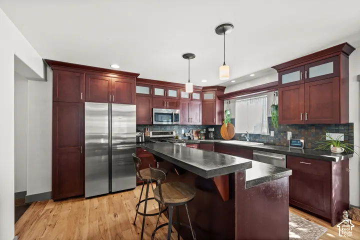 Kitchen featuring wood-finish flooring, dark wood cabinetry, a center island with a dark countertop, and stainless steel appliances