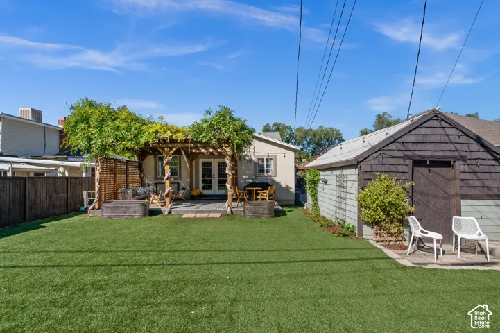 Expansive artificial turf lawn with a large wooden pergola, elevated deck, dual French doors, and a detached structure