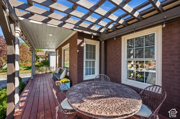Brick exterior with white-framed windows, a covered porch with wood-finish flooring, a wood pergola structure, and recessed lighting