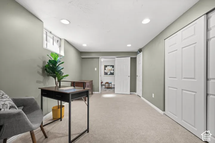 Recessed lighting illuminates the space, featuring light-colored carpeting, a wall-mounted window, and white bi-fold closet doors
